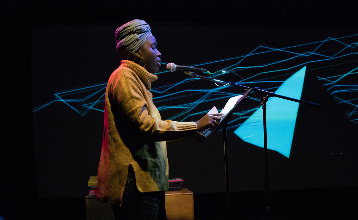Poet Angel Nafix reading in front of a projection of shapes and lines